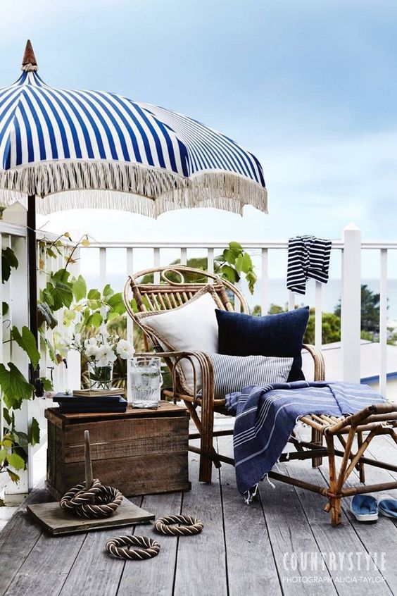 a seaside terrace with a wooden deck, rattan and wooden furniture, bright blue textiles, rope and some greenery