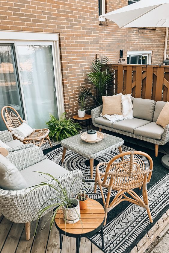 a small beach terrace with neutral wicker furniture, rattan chairs, potted plants and a bold boho rug