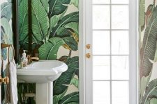 a small tropical powder room with banana leaf wallpaper, a free-standing sink, a basket and gold touches