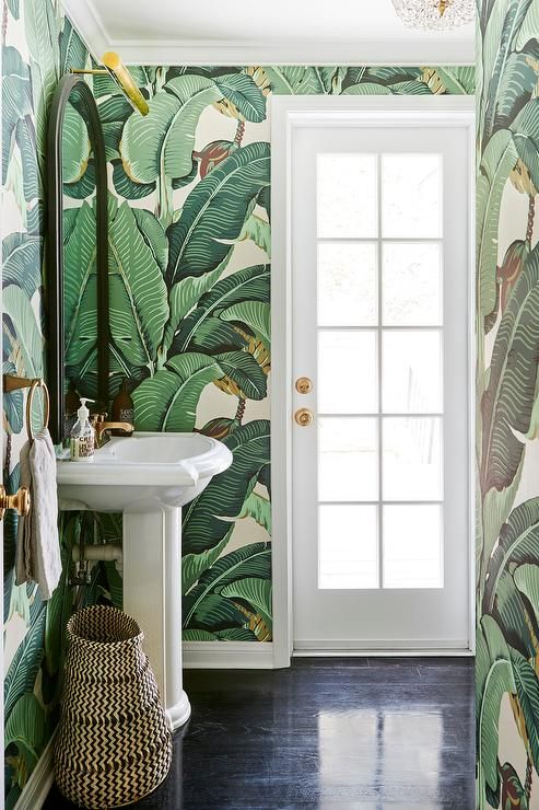 a small tropical powder room with banana leaf wallpaper, a free-standing sink, a basket and gold touches