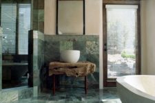 a stunning natural bathroom with green marble tiles, a raw wood slab vanity and wooden touches