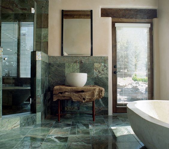 a stunning natural bathroom with green marble tiles, a raw wood slab vanity and wooden touches