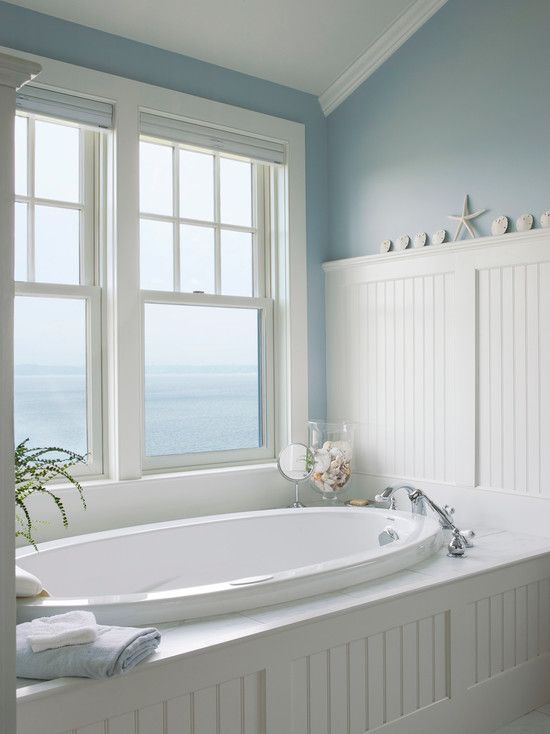 a traditional sea-inspired bathroom done in white and blue, with an oval sunken tub and a gorgeous view to the sea