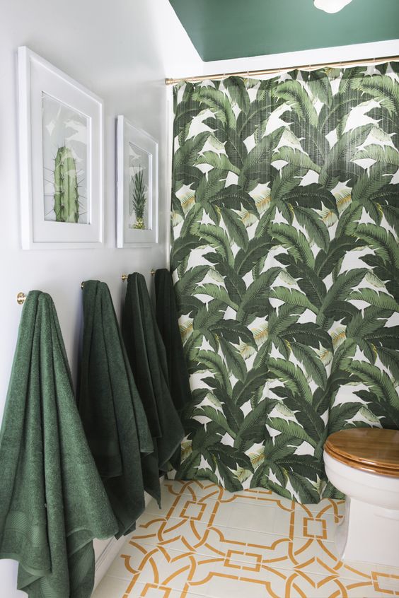 a tropical bathroom in neutrals, with a banana leaf curtain, green towels, a green ceiling and bold artworks