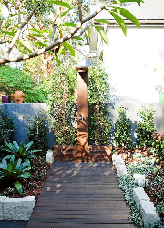 a welcoming outdoor shower done with wood, rocks and planted greenery all around