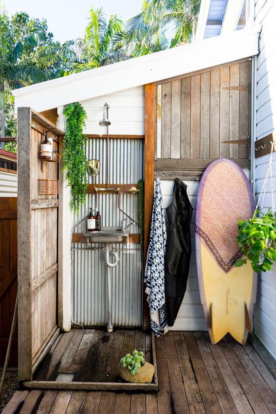 a welcoming outdoor shower with corrugated steel, weathered wood and a surf board