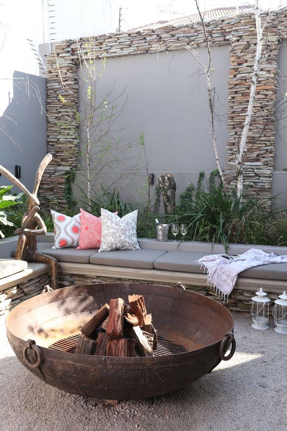 a welcoming outdoor space with a corner bench, a large wrought metal fire bowl, some greenery and whimsical decor