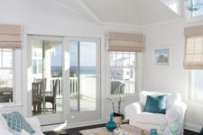 an airy beach living room with woven Roman shades, a wooden table, touches of blue and turquoise, white upholstered furniture