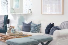 an airy ocean-inspired living room with light blues and navy, printed pillows, light blue stools, artworks and a rattan table