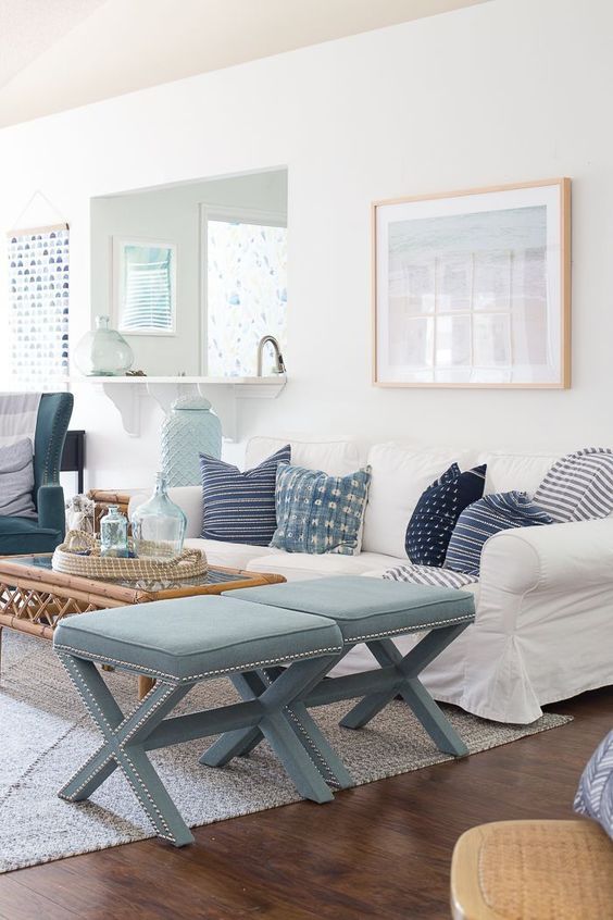 an airy ocean-inspired living room with light blues and navy, printed pillows, light blue stools, artworks and a rattan table