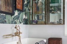 an elegant vintage tropical bathroom with banana leaf wallpaper, a catchy tub, glass and mirror cabinets and artworks