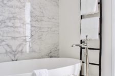 monochromatic chic with a white marble wall, an oval tub, a black ladder and a printed side table