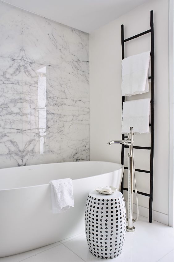 monochromatic chic with a white marble wall, an oval tub, a black ladder and a printed side table