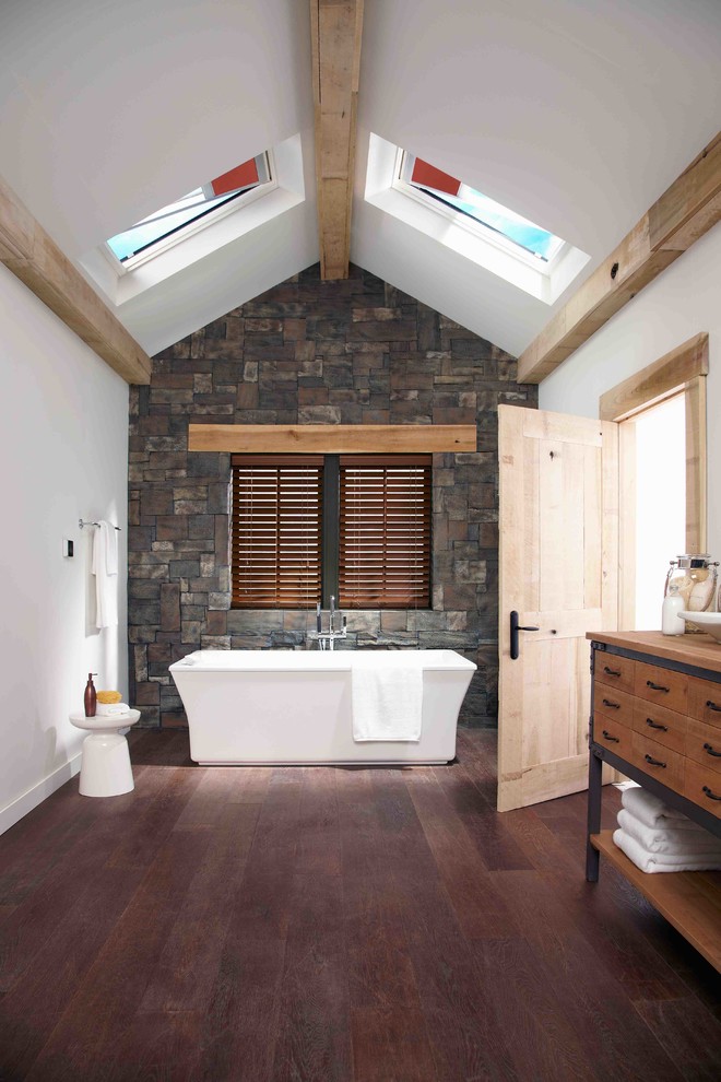a contemporary rustic bathroom with a wooden floor and a stone wall, a wooden vanity (Skylight Specialists, Inc.)