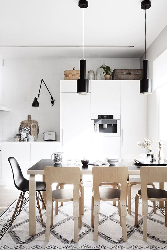 a Nordic kitchen with sleek white cabinets, black lamps, a black table and plywood chairs