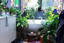 a boho Moroccan bathroom with a colorful curtain, a brugth rug and artwork and lots of potted greenery