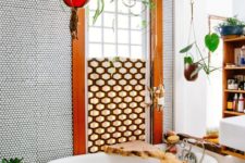 a boho bathroom done with penny tiles, a geometric screen, potted greenery, a clawfoot tub and living edge caddy