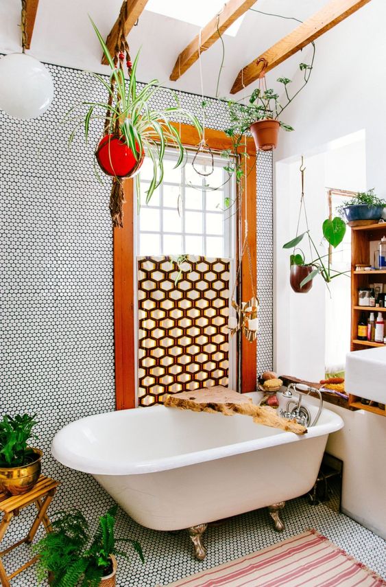 a boho bathroom done with penny tiles, a geometric screen, potted greenery, a clawfoot tub and living edge caddy