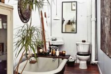 a boho meets rustic bathroom with a stained floor, a black tub, potted greenery, a decorative basket, vintage appliances