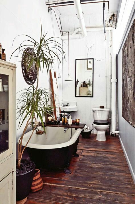 a boho meets rustic bathroom with a stained floor, a black tub, potted greenery, a decorative basket, vintage appliances