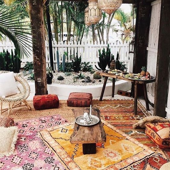a boho patio with colorful printed rugs, cushions, ottomans, rattan and wooden furniture, Moroccan lanterns