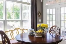a bold vintage dining room with grey walls, a large window, a heavy round table and chairs, decorative plates and a bold yellow rug