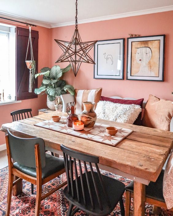 a bright Moroccan dining room with coral walls, a wooden table, mismatching chairs and pillows and a beautiful star-shaped pendant lamp