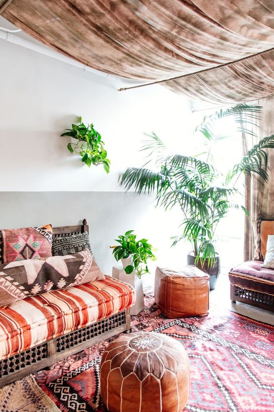 a bright Moroccan living room with colroful textiles, potted plants, a fabric ceiling and a leather ottoman