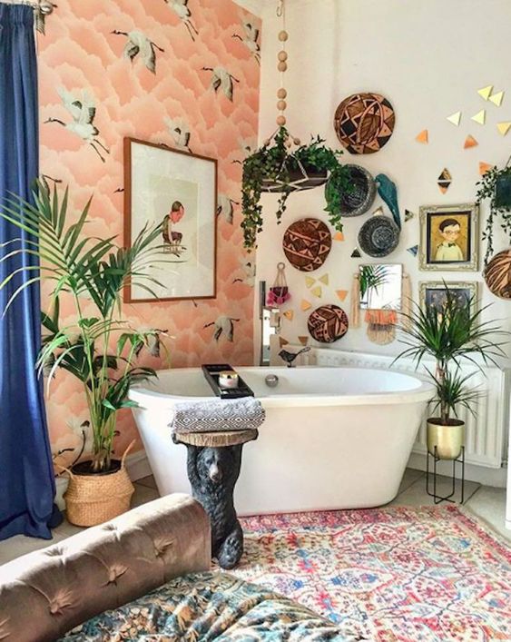 a bright bathroom with a wallpaper wall, boho rugs, decorative baskets, potted plants and artworks