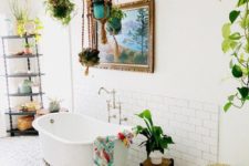 a bright boho bathroom with a mosaic tile floor, boho rugs and towels, potted plant,s a clawfoot tub and an etagere