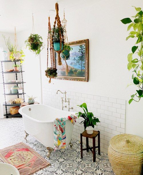 a bright boho bathroom with a mosaic tile floor, boho rugs and towels, potted plant,s a clawfoot tub and an etagere