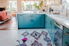 a bright teal kitchen with wooden uppers and a colorful fringe boho rug