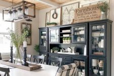 a chic farmhouse dining area with a black and glass buffet, signs, a white table and checked chairs and a frame chandelier