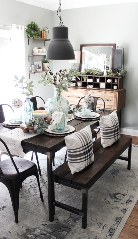 a chic farmhouse dining space with a wooden buffet, a dark stained wooden dining set, a metal lamp and lots of greenery