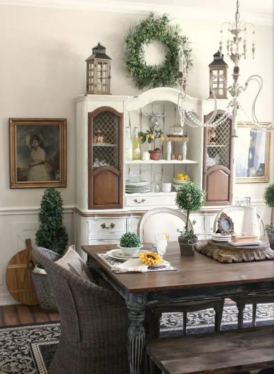 a classic farmhouse dining space with a shabby chic dining set, wicker chairs, a white and brown buffet and beautiful artworks