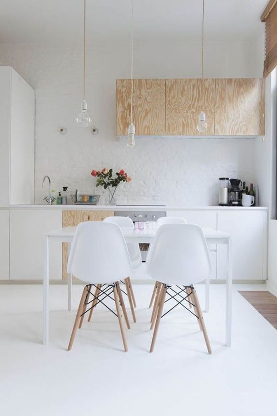 a contemporary Scandinavian kitchen with white and plywood cabinets, bulbs hanging from above and a sleek dining set