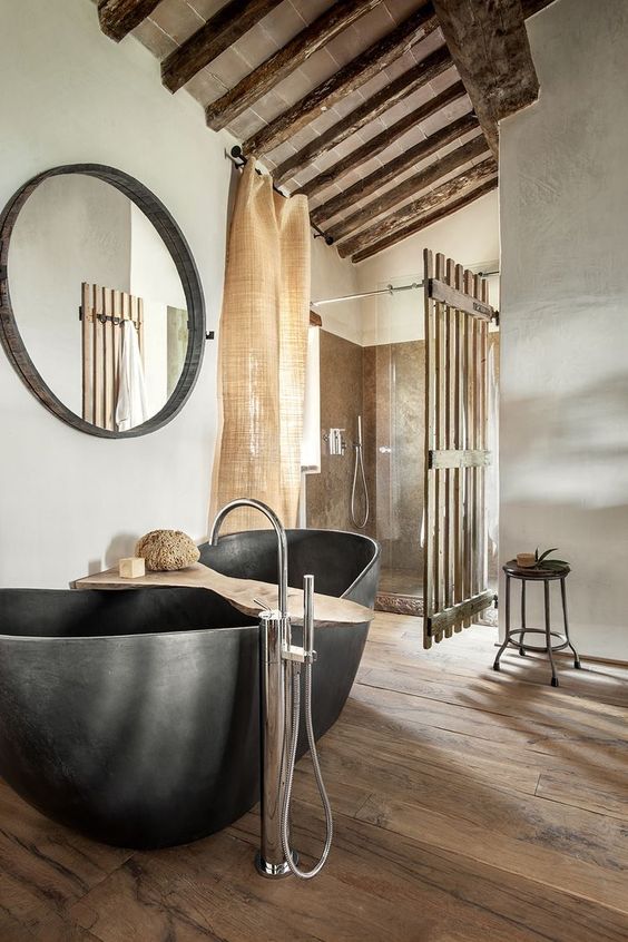 a contemporary meets industrial bathroom with a stone tub, burlap curtains and much wood