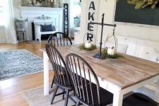 a cute farmhouse dining nook with a chalkboard, a greenery wreath, a wooden dining table, black chairs and a chandelier