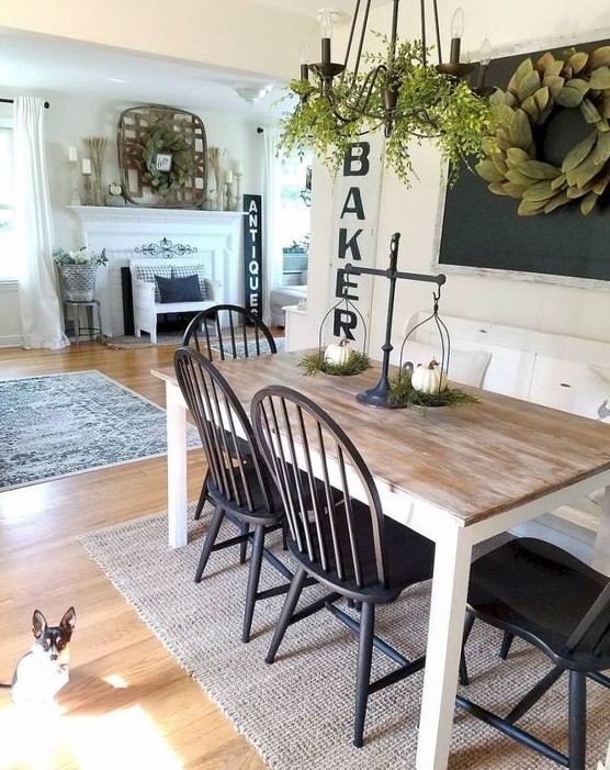 a cute farmhouse dining nook with a chalkboard, a greenery wreath, a wooden dining table, black chairs and a chandelier