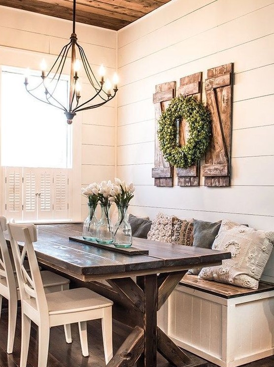 a cute neutral farmhouse dining nook with a built-in bench, a wooden table, white chairs and a metal chandelier