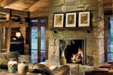 a dark rustic living room with a stone clad fireplace, wooden beams on the ceiling and leather furniture that make the space cozier