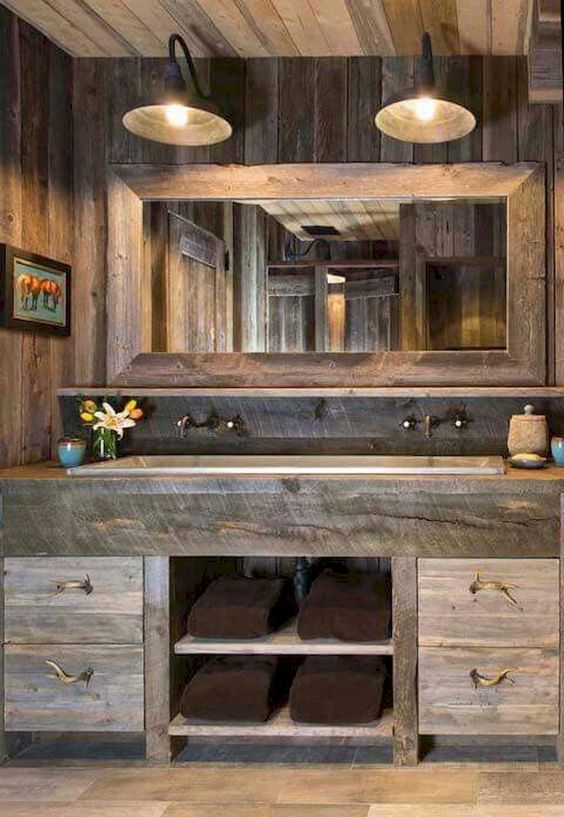 a farmhouse bathroom of weathered wood, with a large mirror and wall lamps