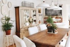 a farmhouse dining area with stained furniture, white covered chairs, potted greenery and white pendant lamps