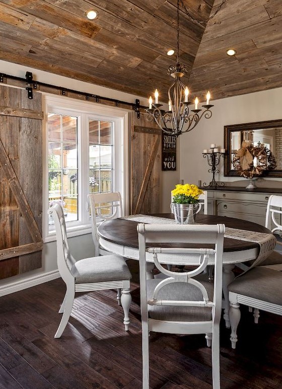 a farmhouse wooden dining area with a statement stained wood ceiling and shutters, vintage white furniture and a framed mirror