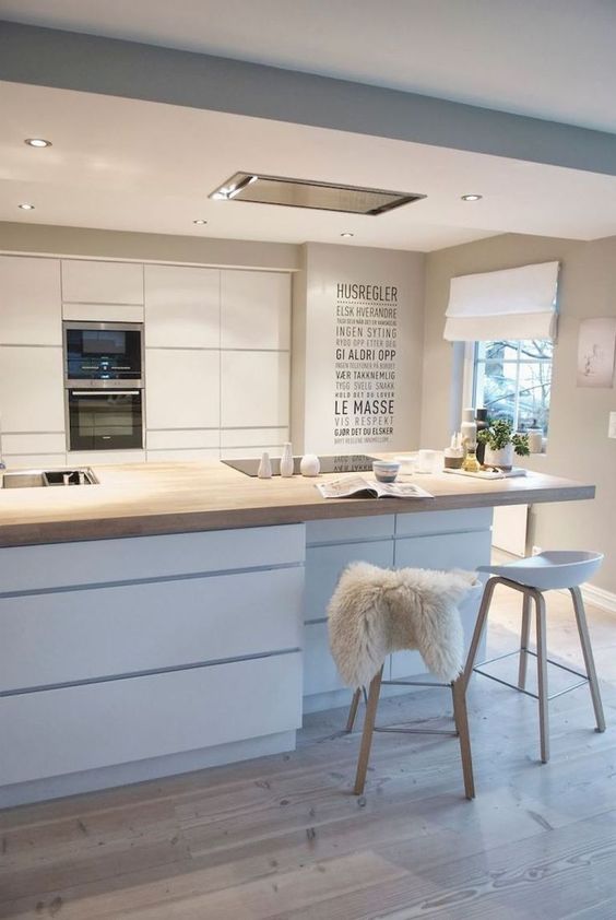 a glam Scandinavian kitchen with sleek cabinets, a storage kitchen island with a woodne countertop, wooden stools and lights