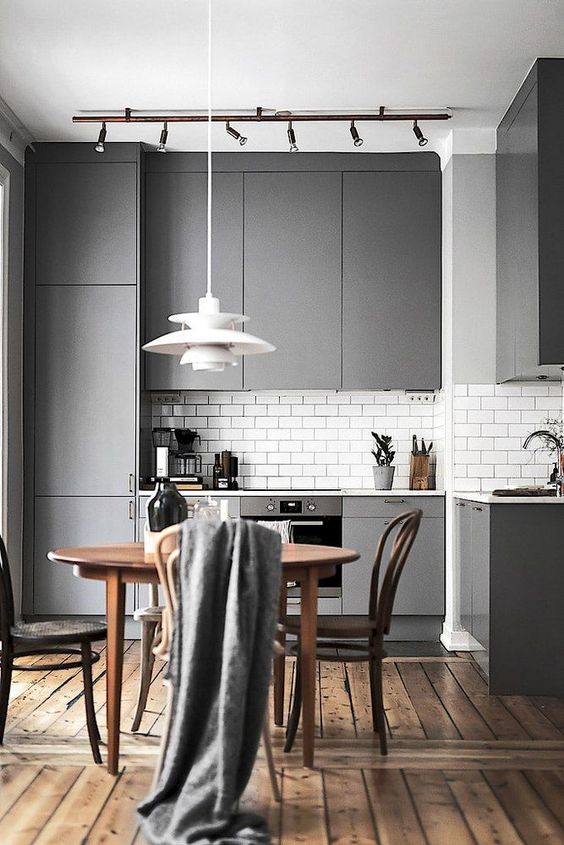 a laconic minimalist kitchen with grey sleek cabinets, a wooden dining set, a pendant lamp and additional lights