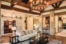 a large rustic living room with an attic ceiling and beams, stone clad pillars and a stained wooden floor