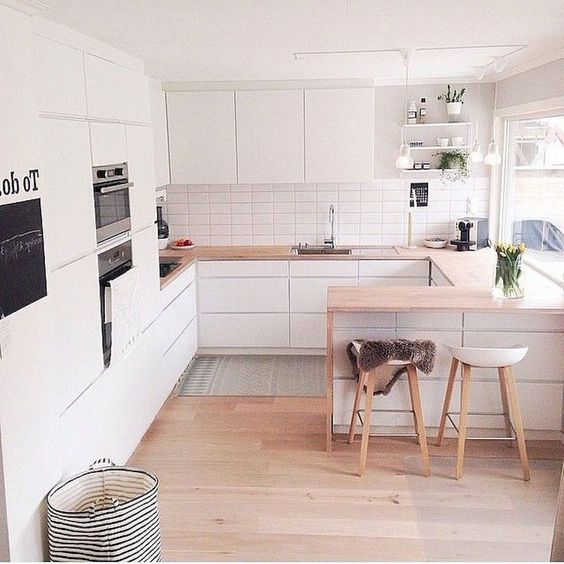 a minimalist Scandinavian kitchen with sleek white cabinets, light staiend countertops, stools and built-in appliances