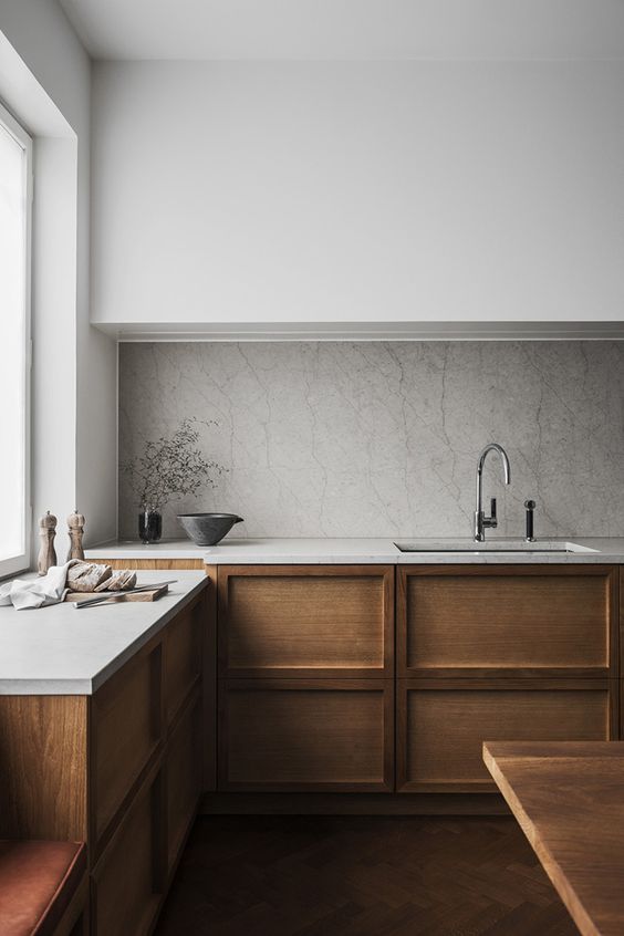 a minimalist Scandinavian kitchen with sleek white uppers, paneled wood lower cabinets, a stone backsplash and countertops