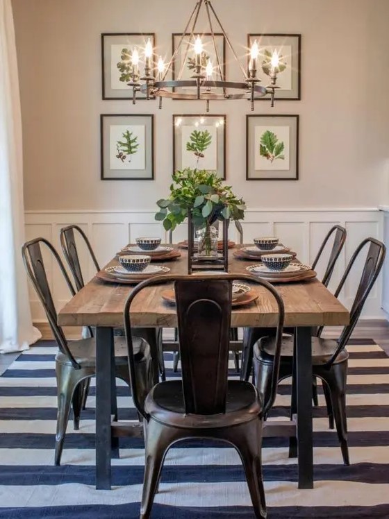 a modern country dining zone with a stained table, metal chairs, a striped rug, a large metal chandelier and an organic gallery wall